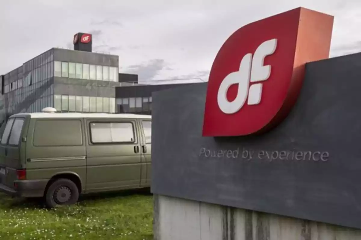 Edificio de oficinas con logotipo rojo y blanco de "df" en primer plano y una furgoneta verde estacionada en el césped.