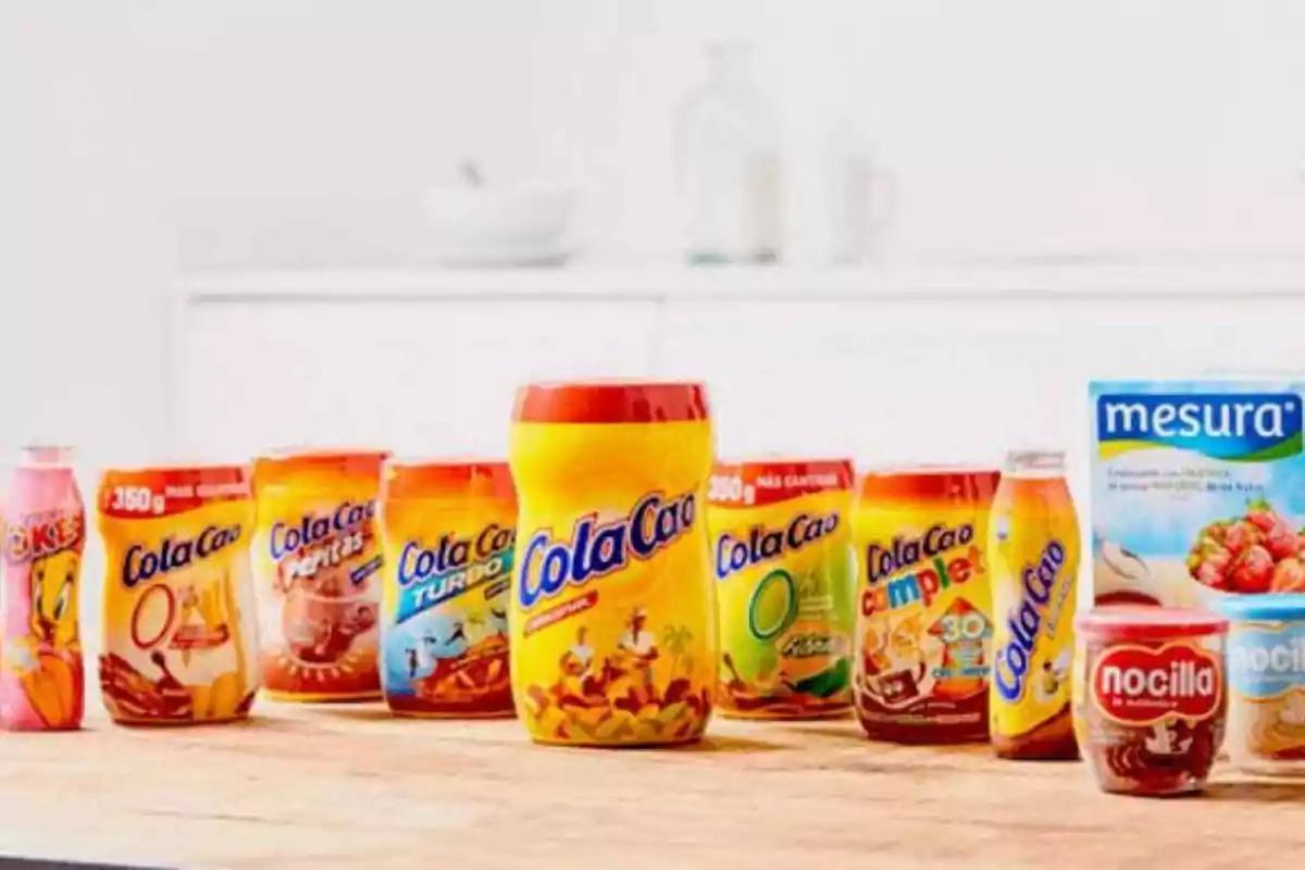 Varios productos de la marca ColaCao, Nocilla y Mesura sobre una mesa de madera en una cocina.