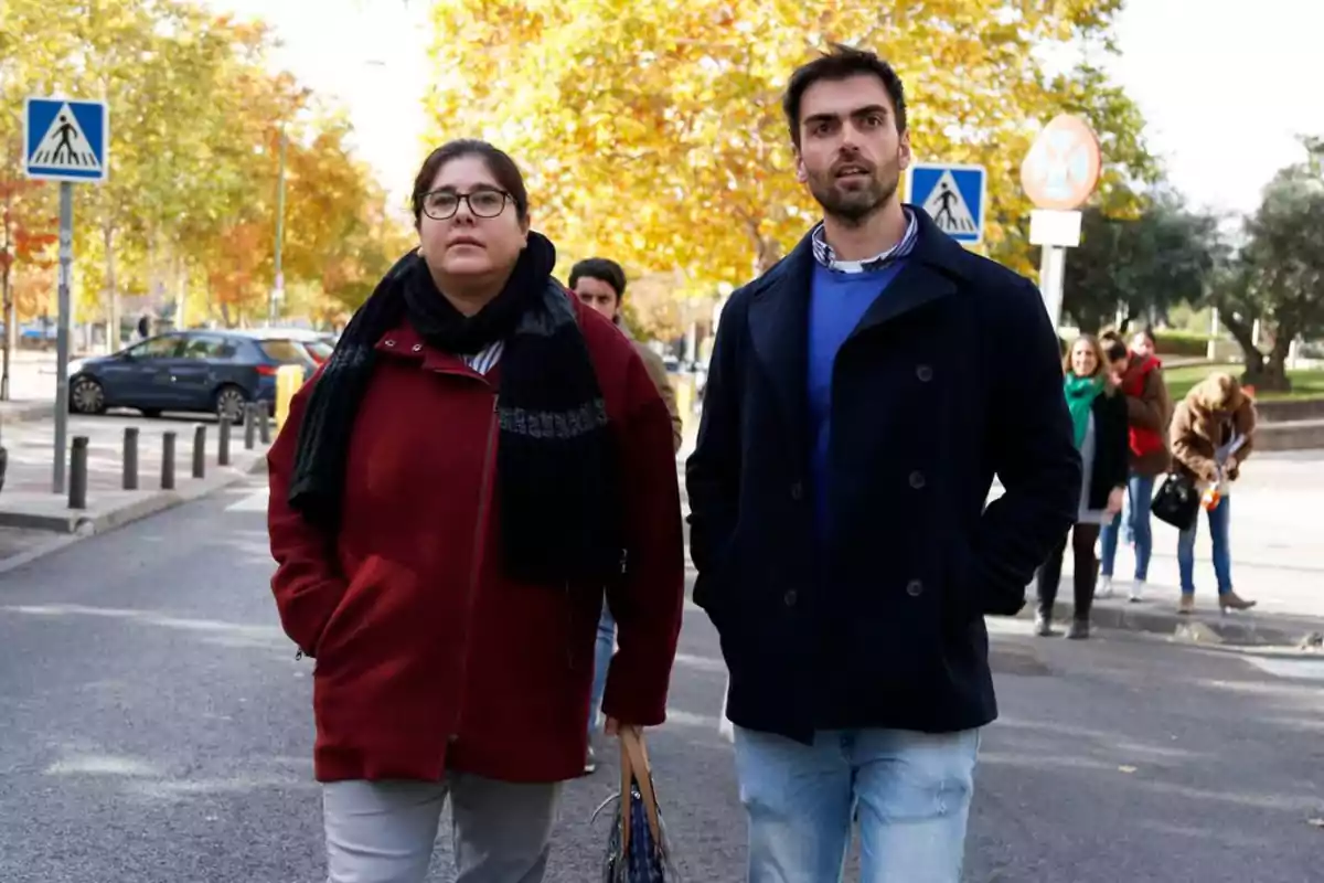 Dos personas caminando por la calle en un día soleado de otoño con árboles de hojas amarillas y otras personas al fondo Dos personas caminando por la calle en un día soleado de otoño con árboles de hojas amarillas y otras personas al fondo