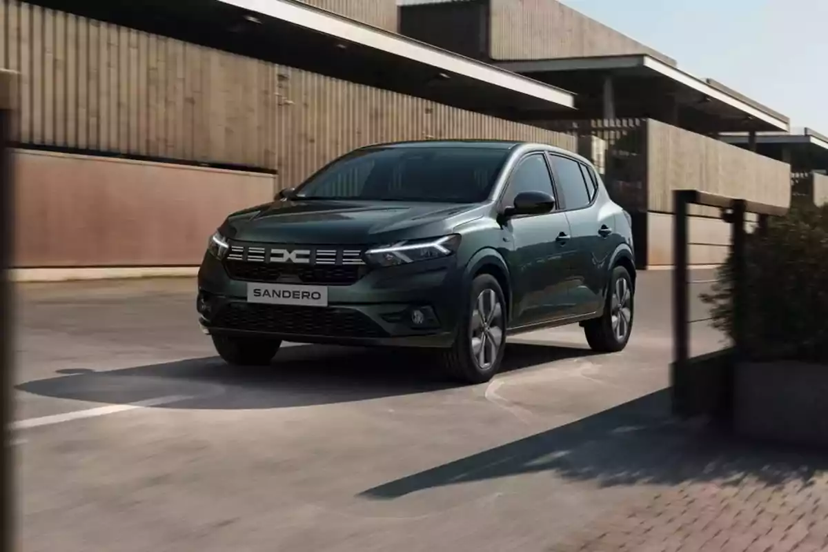 Un automóvil Dacia Sandero de color oscuro circulando por una calle urbana con edificios modernos al fondo.