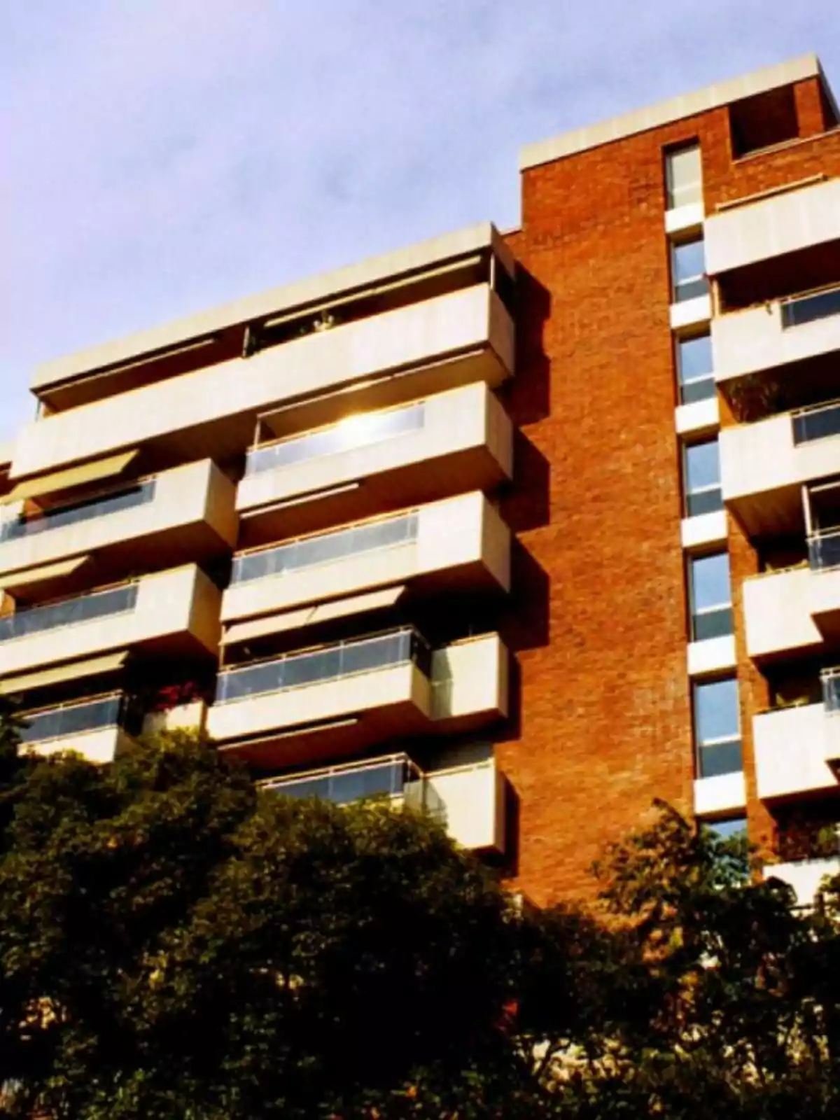 Edificio de apartamentos de ladrillo con balcones y árboles en primer plano.