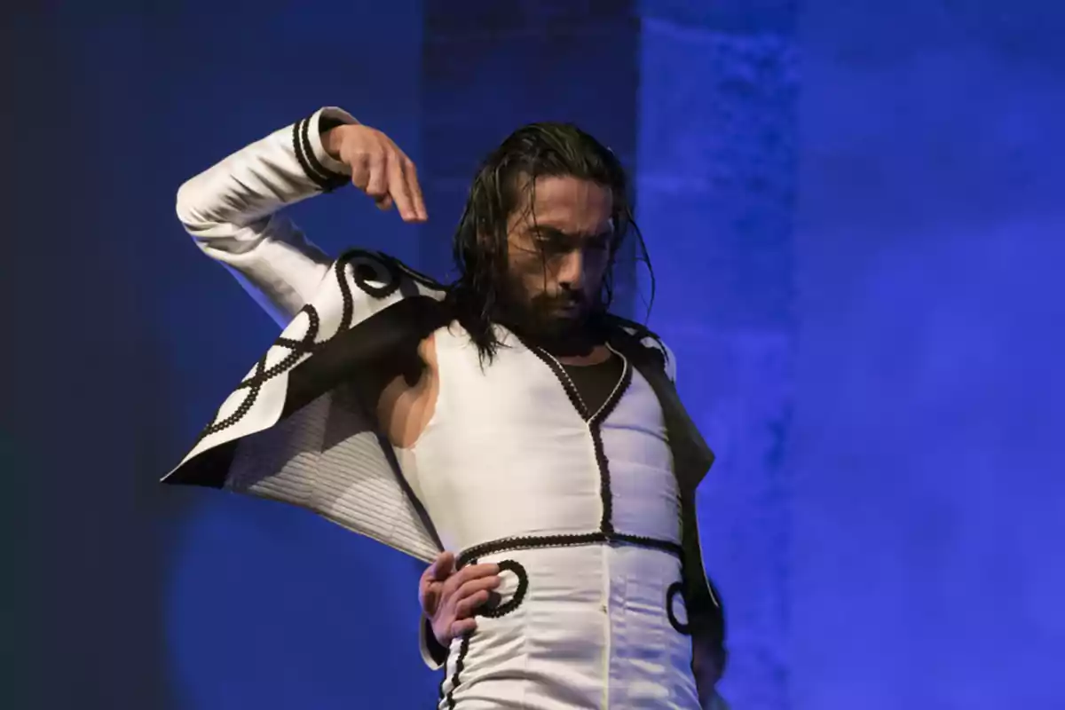 Bailarín de flamenco con traje blanco y negro en una actuación con fondo azul.