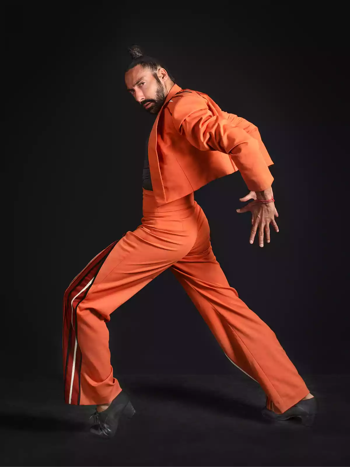 Persona con traje naranja realizando una pose de baile en un fondo oscuro.