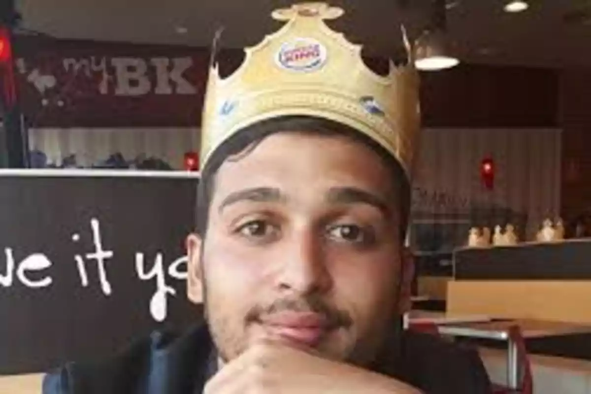 Joven con corona de papel sentado en un restaurante de comida rápida Joven con corona de papel sentado en un restaurante de comida rápida