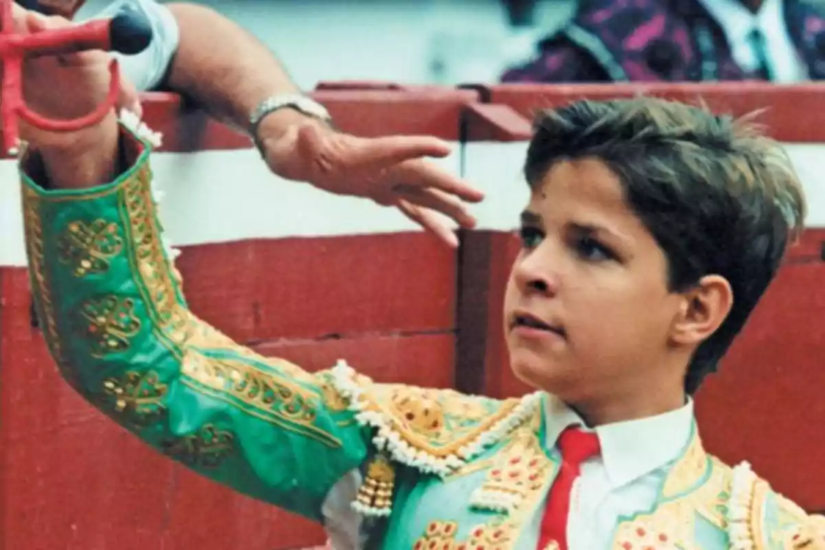 Joven torero vestido con traje verde y dorado en una plaza de toros.