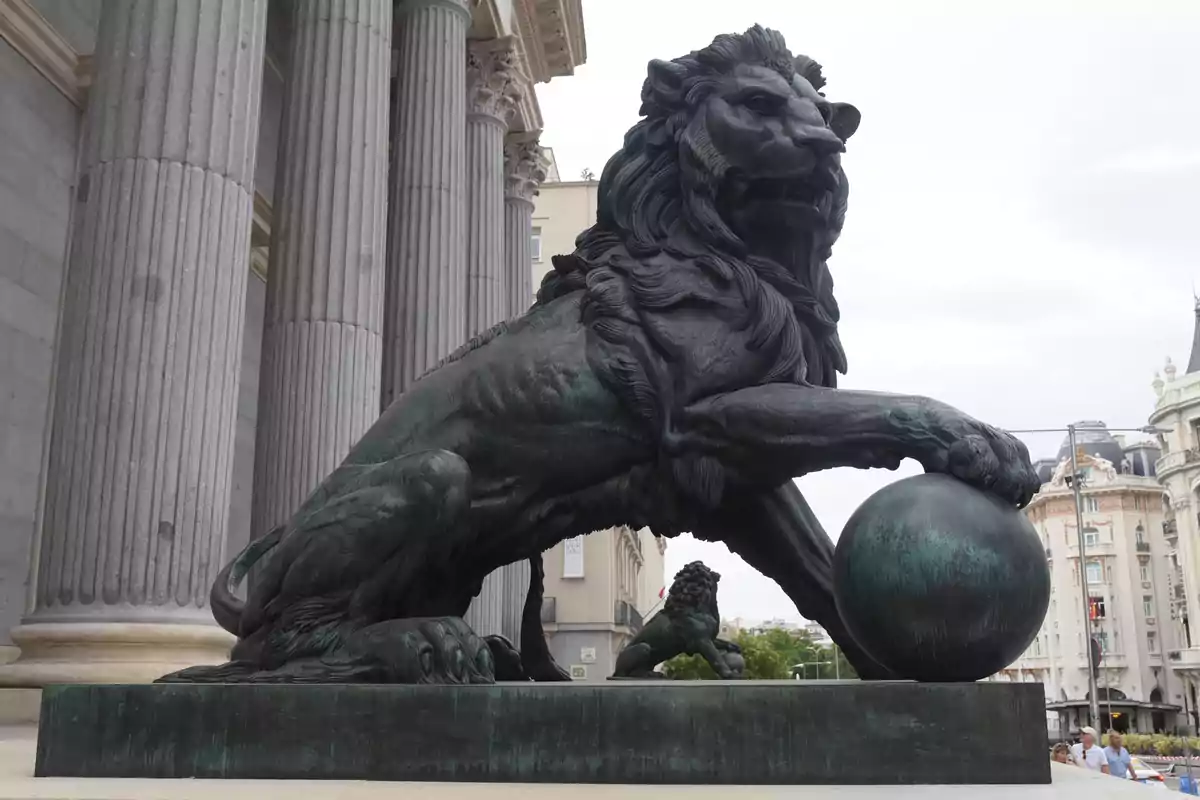 Escultura de un león con una esfera en la entrada de un edificio con columnas en Madrid.