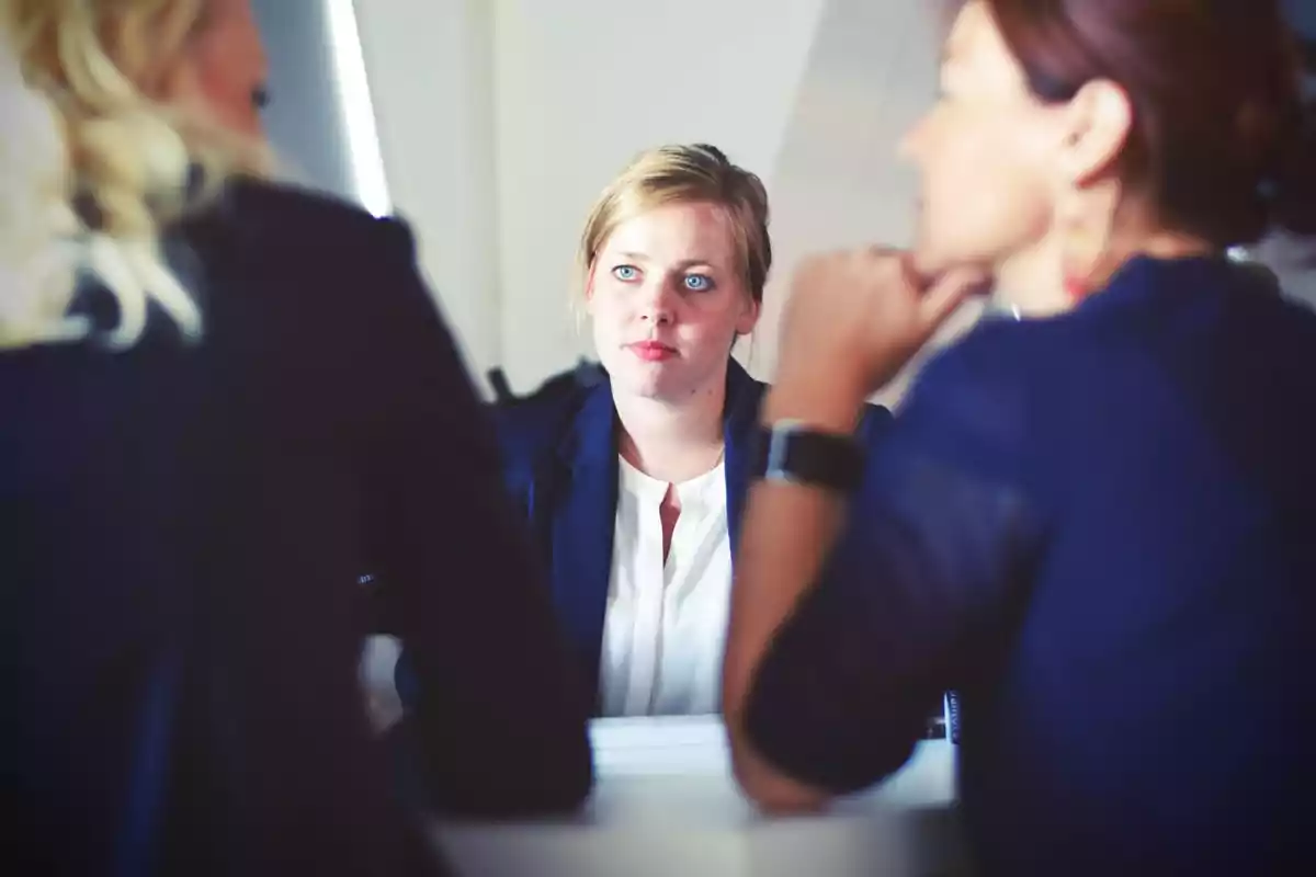 Tres mujeres vestidas de manera formal conversan en una oficina durante una reunión de trabajo