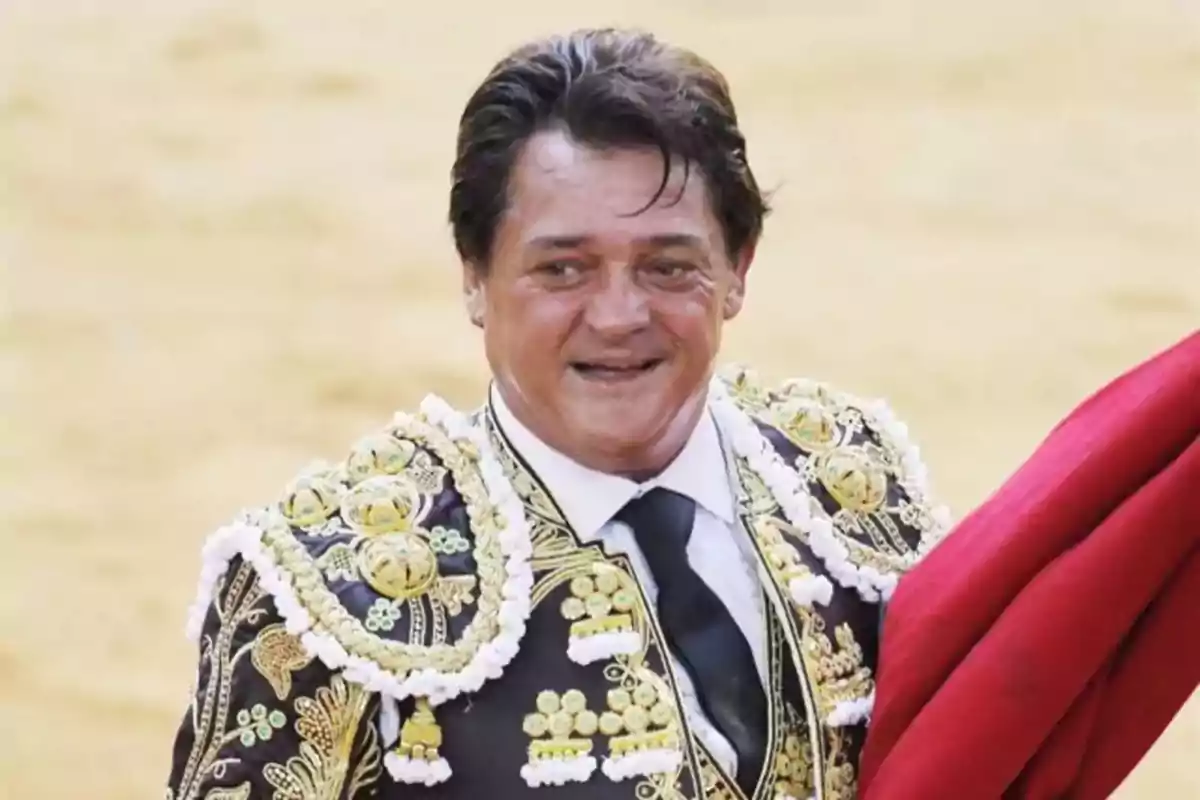 Un torero sonriente con traje de luces y una capa roja en la mano.