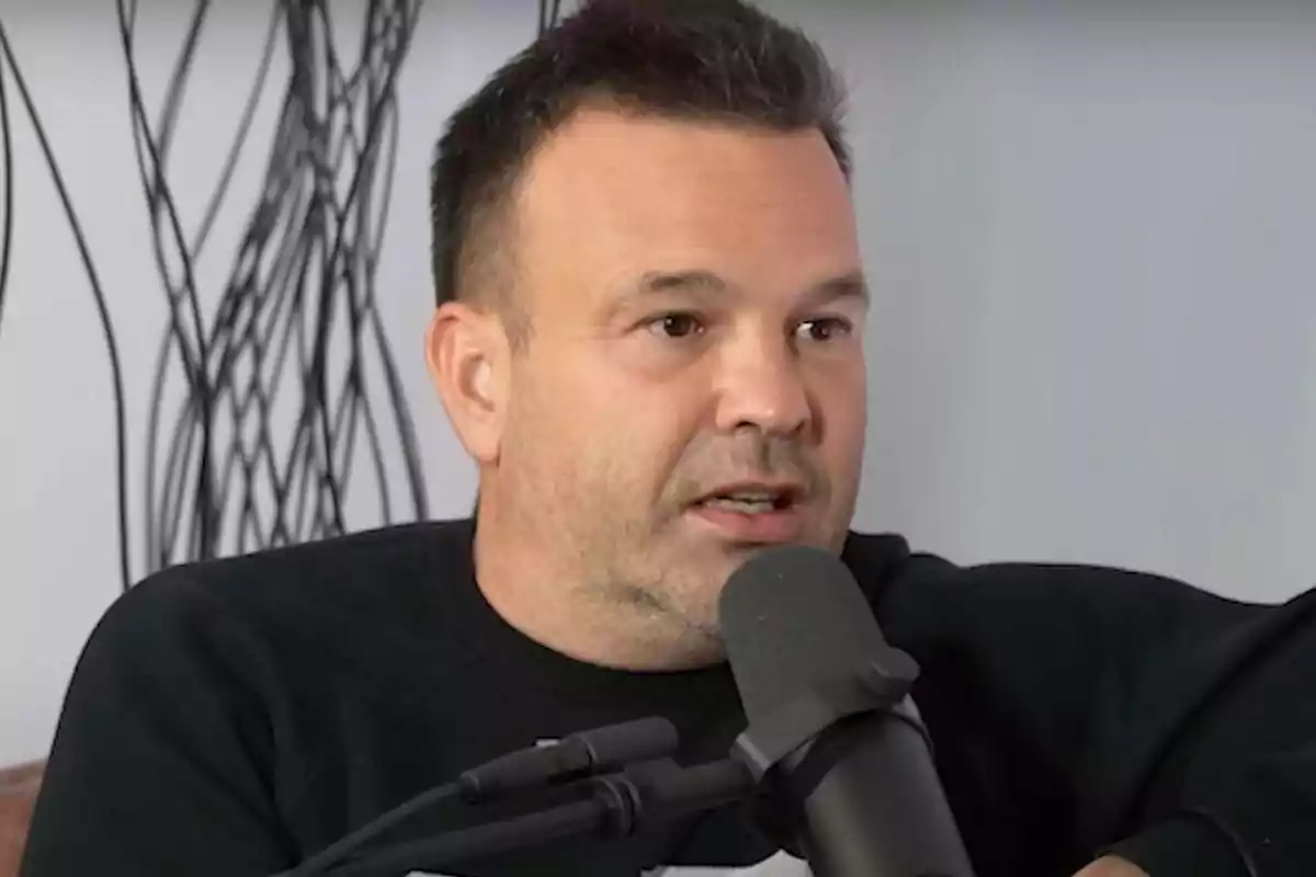 Un hombre hablando frente a un micrófono con un fondo de decoración abstracta.