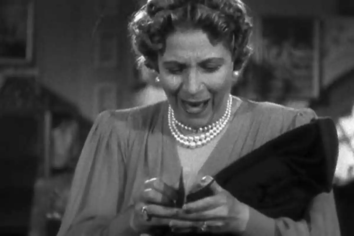 Una mujer mayor con expresión de sorpresa o emoción mira el contenido de una billetera en una escena en blanco y negro. Una mujer mayor con expresión de sorpresa o emoción mira el contenido de una billetera en una escena en blanco y negro.
