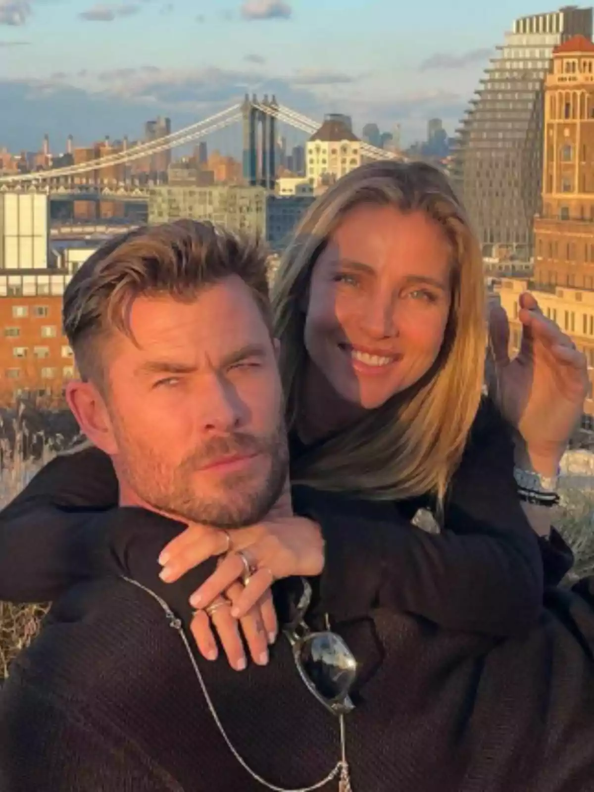 Elsa Pataky y Chris Hemsworth abrazados y sonrientes al aire libre con un puente y edificios de ciudad al fondo. Elsa Pataky y Chris Hemsworth abrazados y sonrientes al aire libre con un puente y edificios de ciudad al fondo.