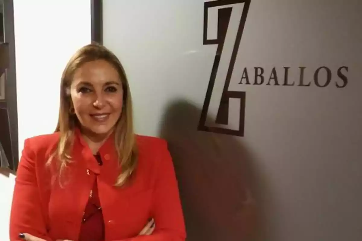 Una mujer con chaqueta roja está de pie frente a una pared con el logotipo y el nombre 