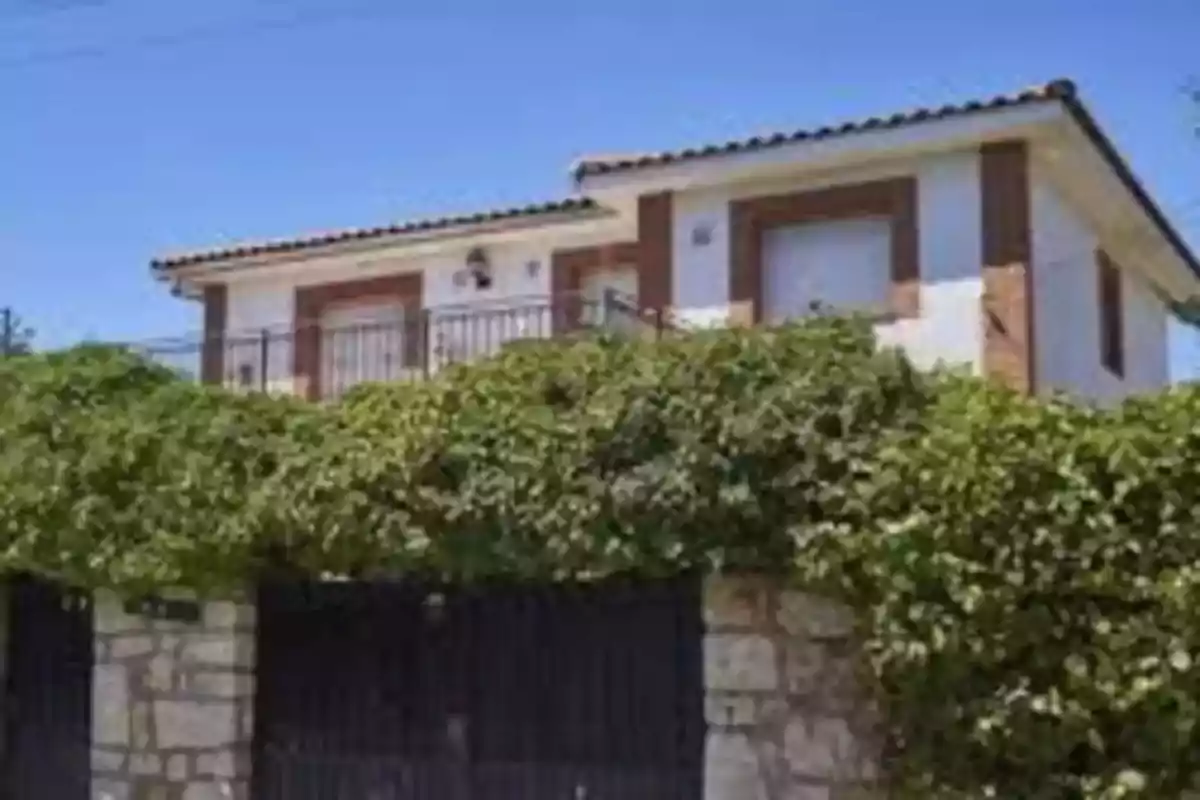 Casa de dos pisos con techo de tejas y enredaderas cubriendo la cerca frontal.