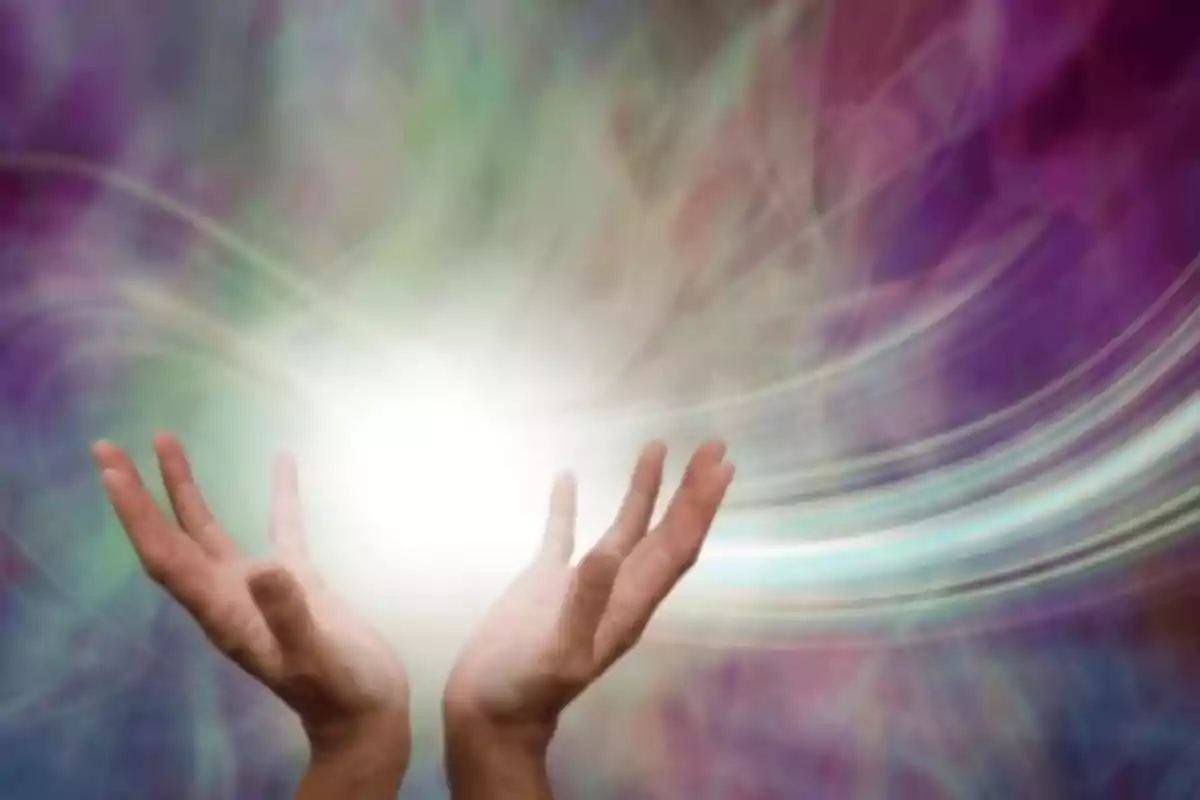 Manos abiertas hacia una luz brillante con un fondo de colores difuminados.