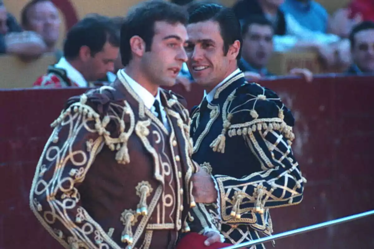 Enrique Ponce y Joselito vestidos de torero y hablando en una plaza de toros.