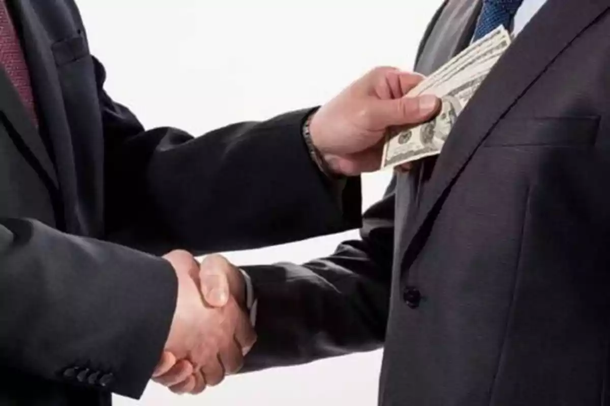 Dos personas de negocios estrechándose la mano mientras una de ellas recibe dinero.