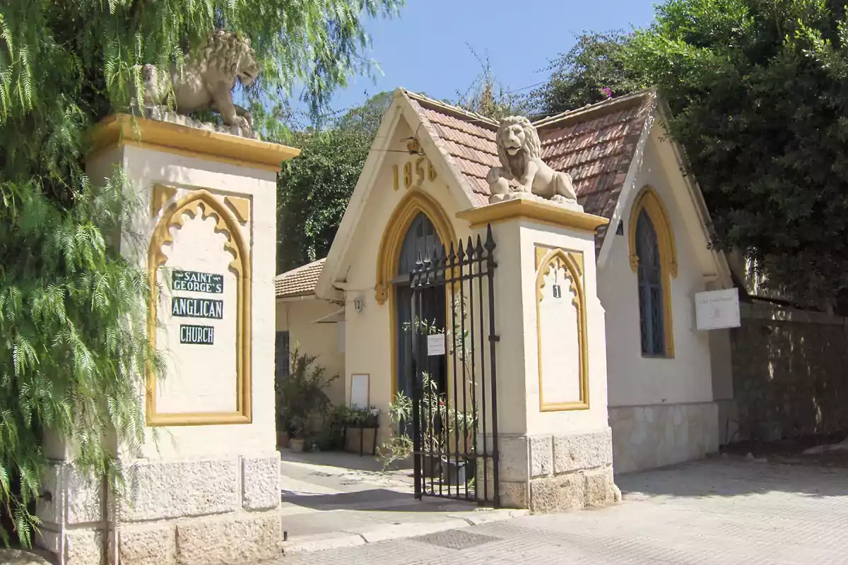 Entrada de la iglesia anglicana de San Jorge con esculturas de leones sobre pilares y un portón de hierro forjado.