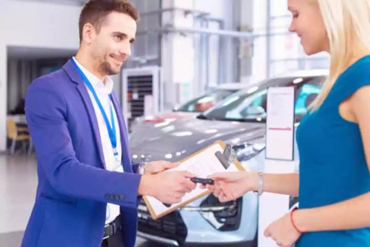 Un vendedor de autos entregando las llaves a una clienta en una concesionaria.