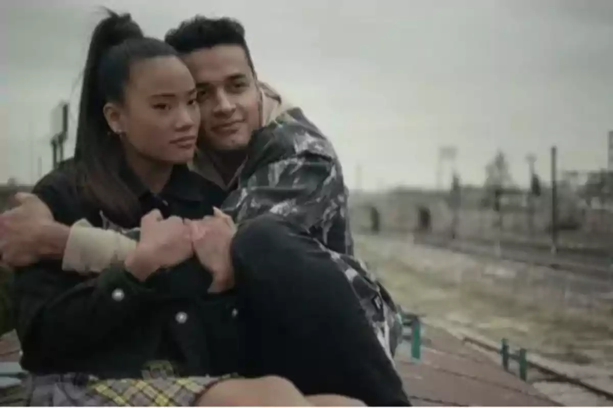 Una pareja joven se abraza mientras está sentada al aire libre cerca de unas vías de tren. Una pareja joven se abraza mientras está sentada al aire libre cerca de unas vías de tren.