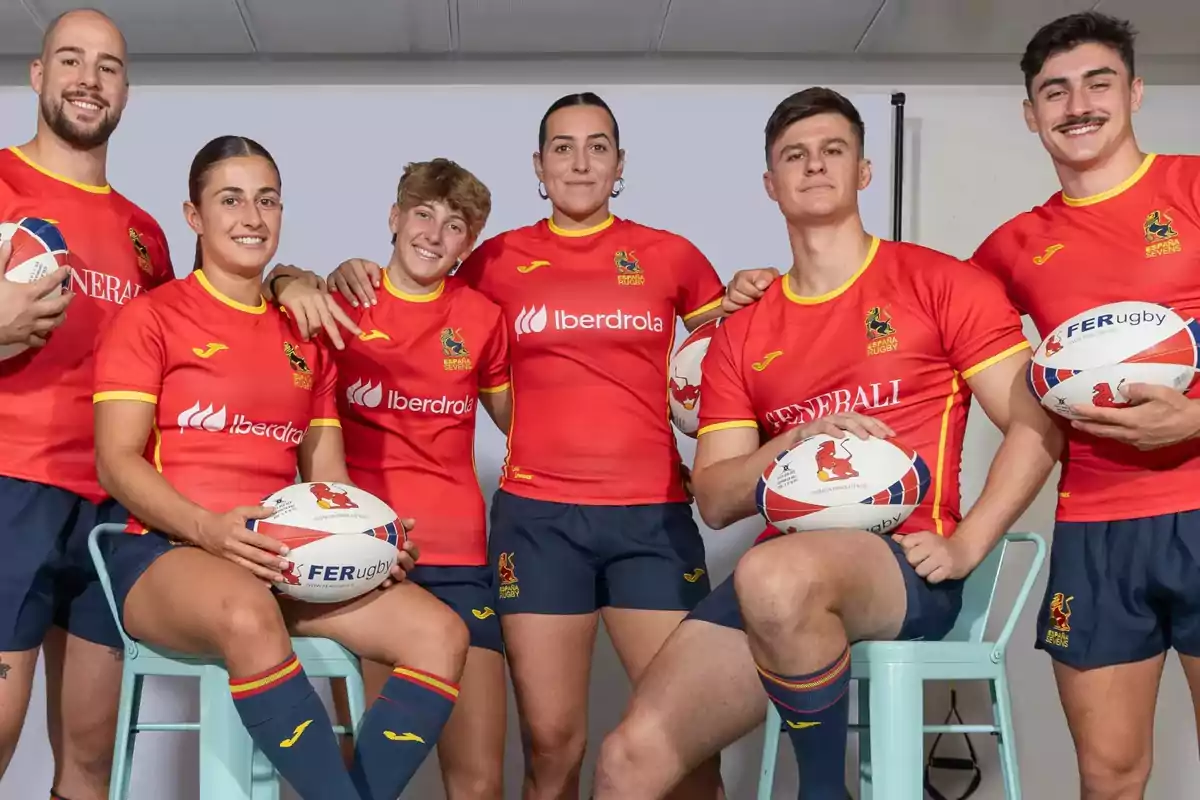 Un grupo de jugadores de rugby, tanto hombres como mujeres, posan juntos con uniformes rojos y balones de rugby.