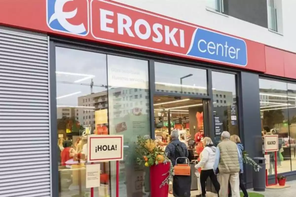 Entrada de una tienda Eroski Center con personas entrando y un cartel de bienvenida.