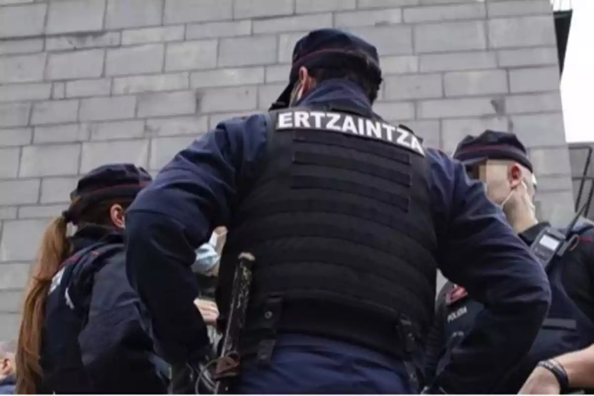 Grupo de agentes de la Ertzaintza conversando frente a un edificio de ladrillos grises