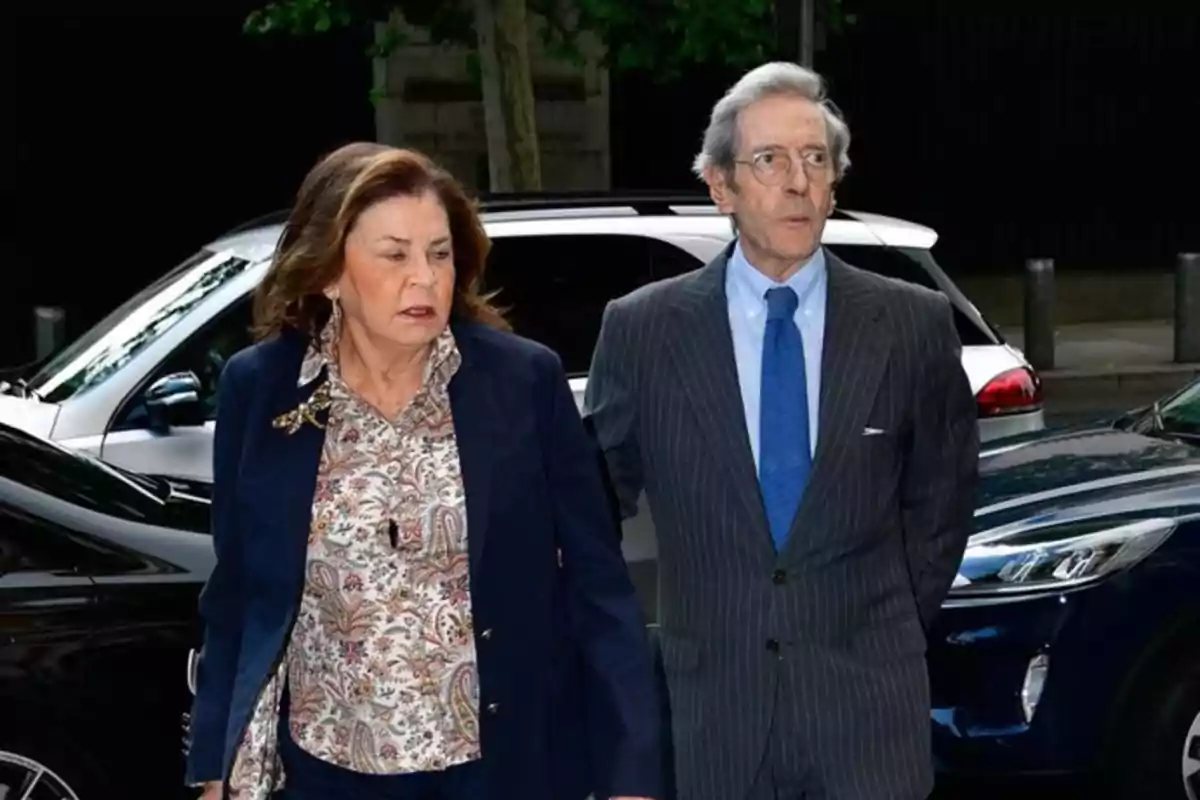 Una mujer y un hombre mayores caminando juntos en la calle, ambos vestidos de manera formal, con coches estacionados a su alrededor. Una mujer y un hombre mayores caminando juntos en la calle, ambos vestidos de manera formal, con coches estacionados a su alrededor.