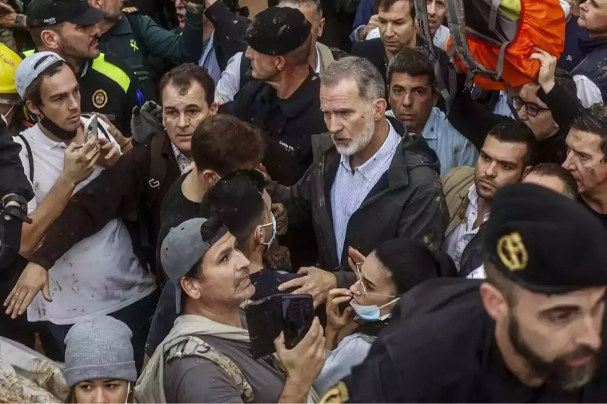 Un grupo de personas rodea a un hombre de cabello canoso y barba en un evento concurrido.