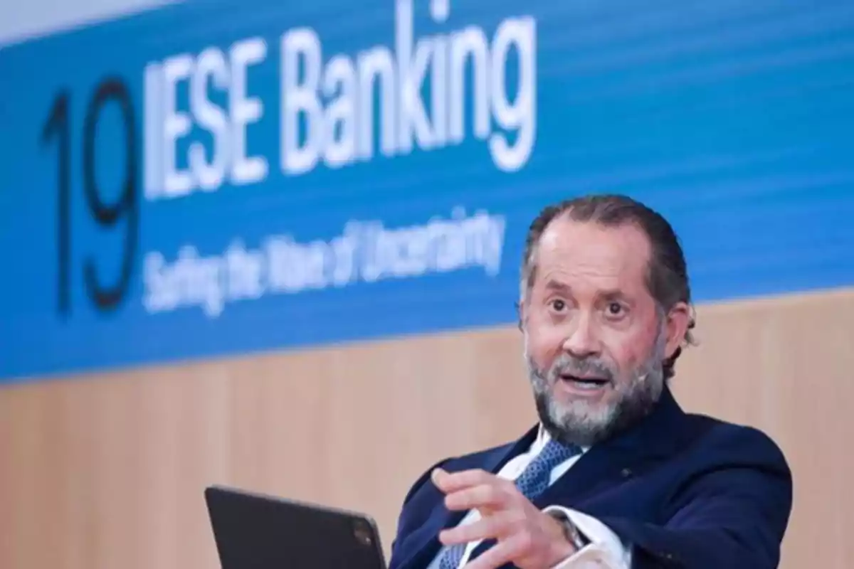 Un hombre hablando en un evento de IESE Banking con un fondo azul.