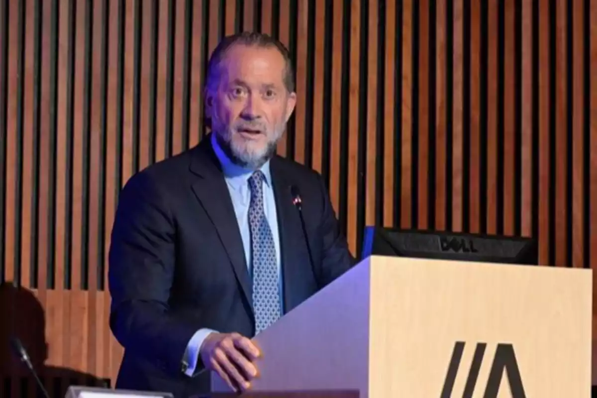 Hombre de traje hablando en un podio de madera con fondo de paneles verticales