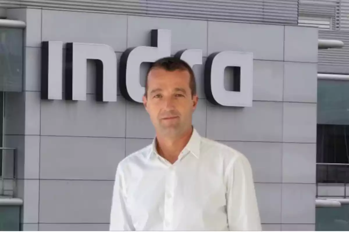 Un hombre con camisa blanca frente a un edificio con el logo de Indra.