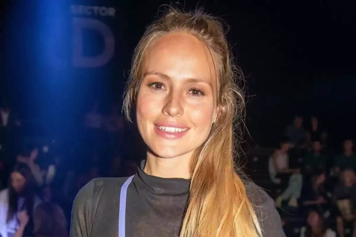 Una persona con cabello largo y rubio sonriendo en un evento con un fondo oscuro y luces brillantes. Una persona con cabello largo y rubio sonriendo en un evento con un fondo oscuro y luces brillantes.