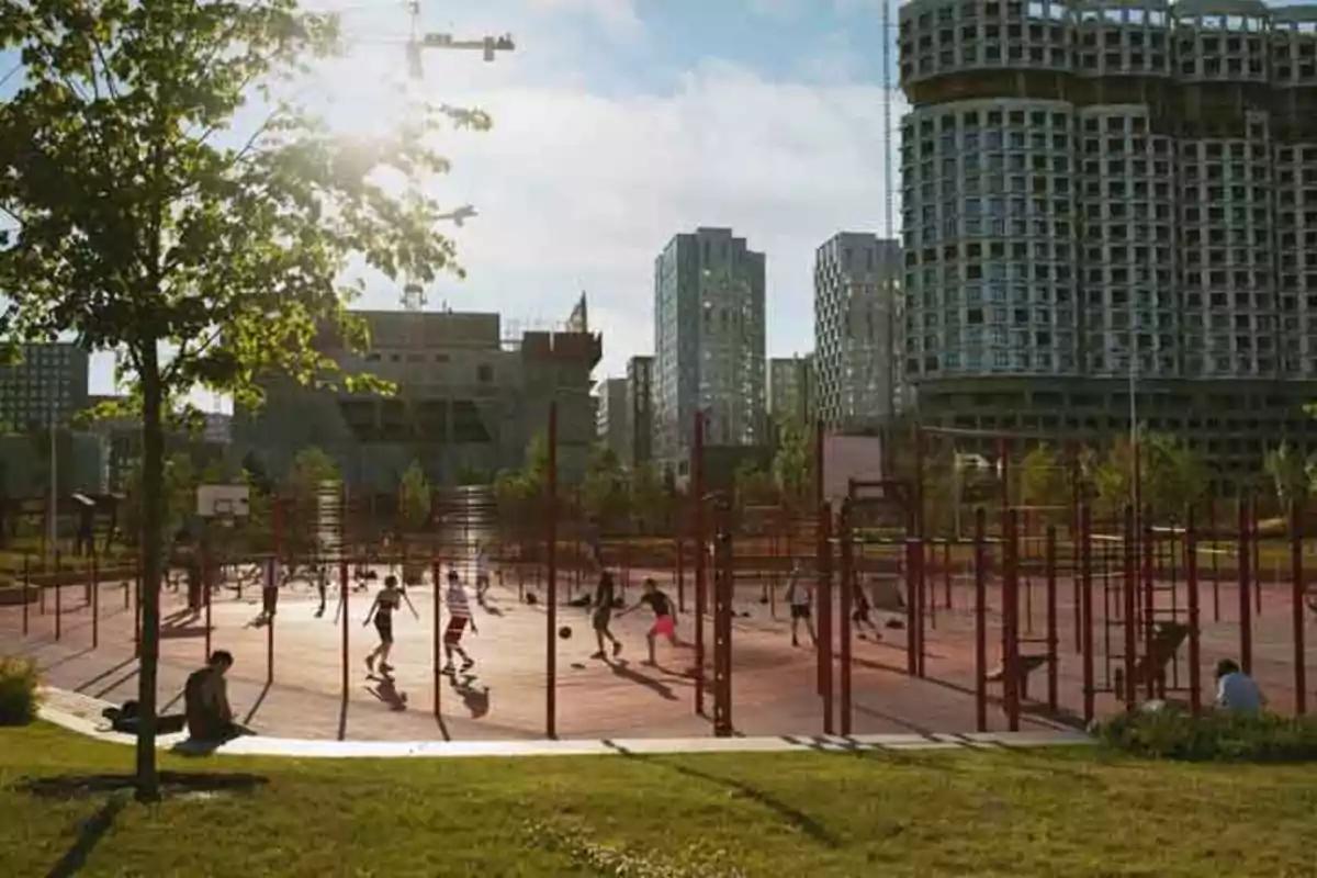 Personas jugando en una cancha de baloncesto al aire libre en un parque urbano con edificios altos al fondo.