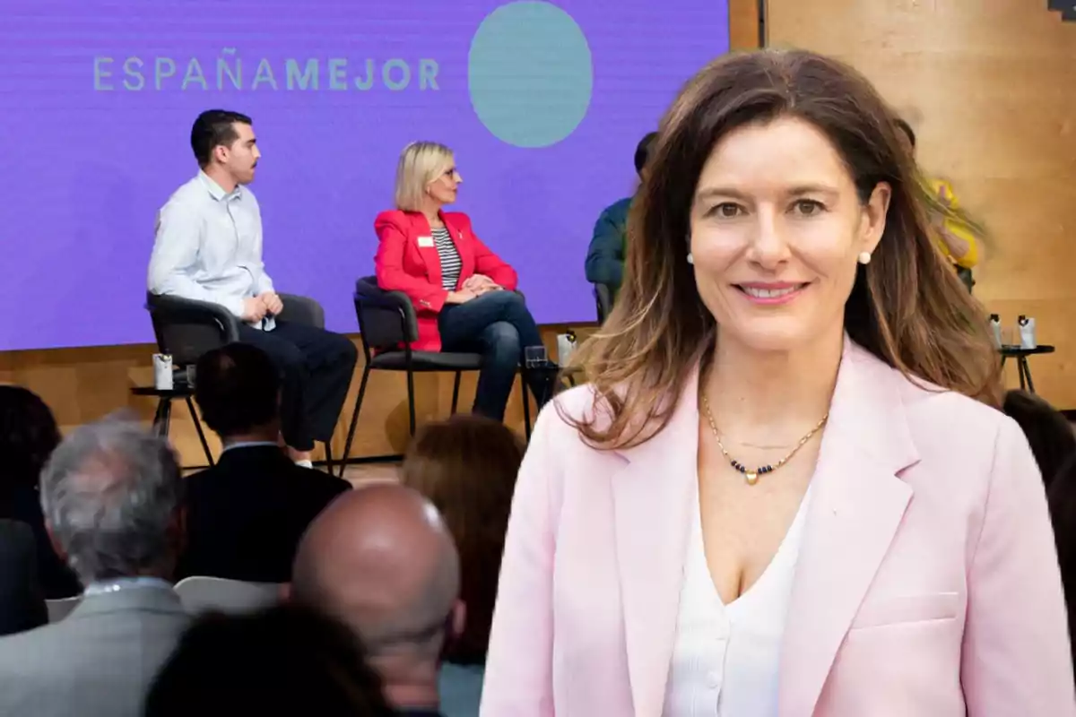 Una mujer sonriente en primer plano con un fondo de personas sentadas en un escenario durante un evento con el texto "ESPAÑA MEJOR" en la pantalla.