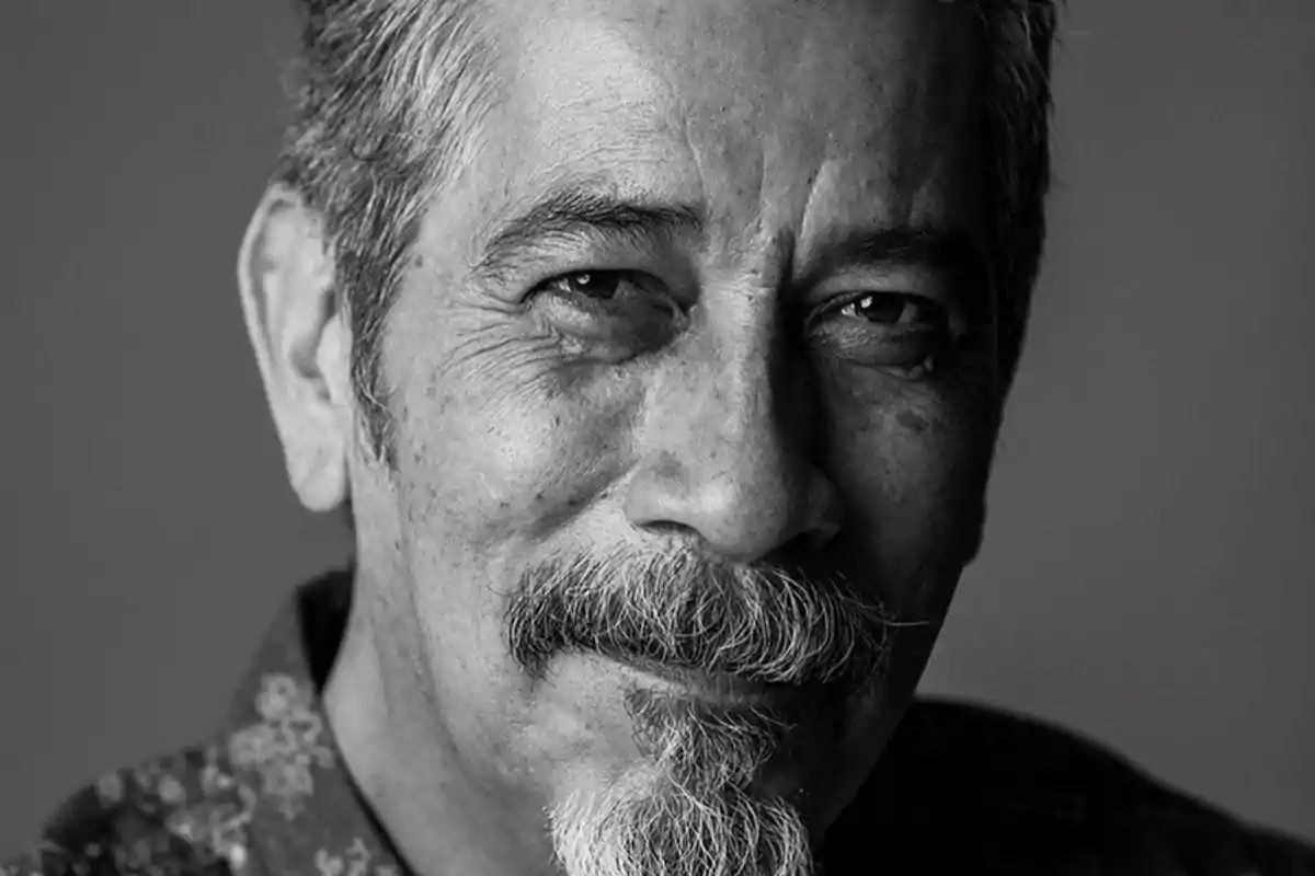 Un hombre mayor con barba y bigote sonríe ligeramente en una fotografía en blanco y negro.