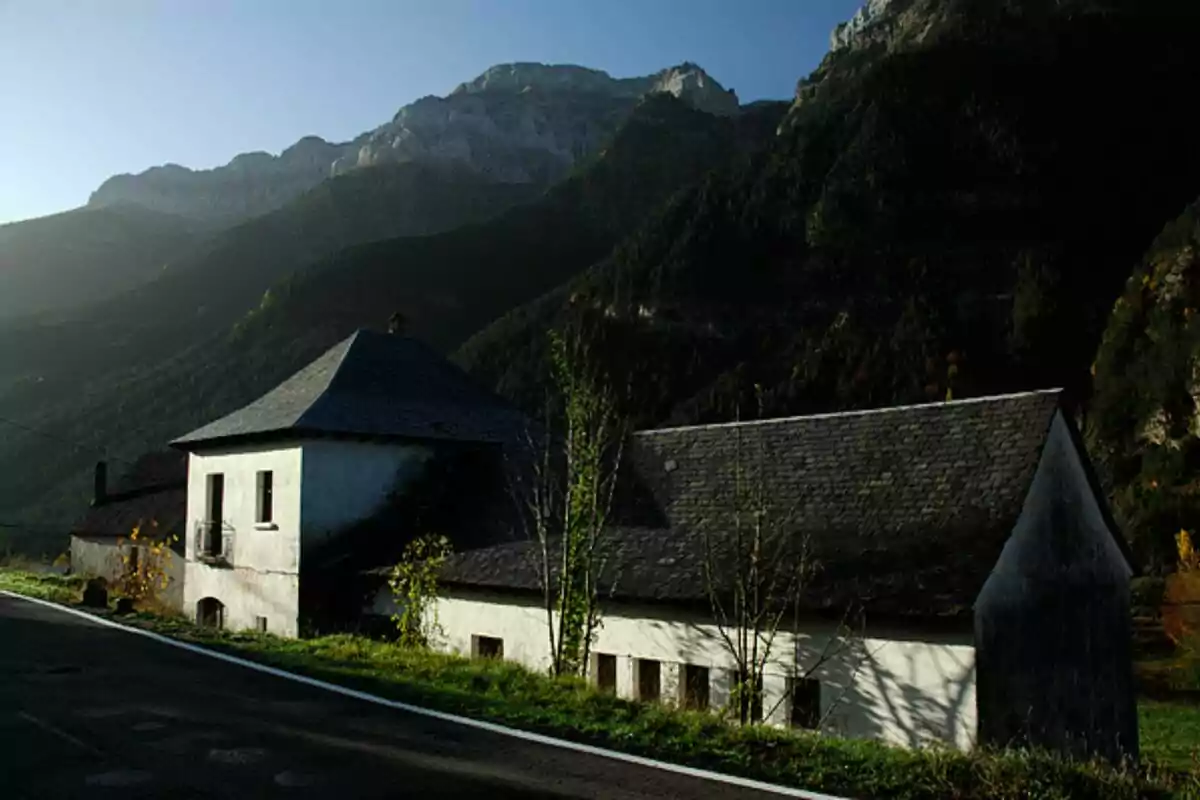 Casa rural con tejado de pizarra en un paisaje montañoso al atardecer.