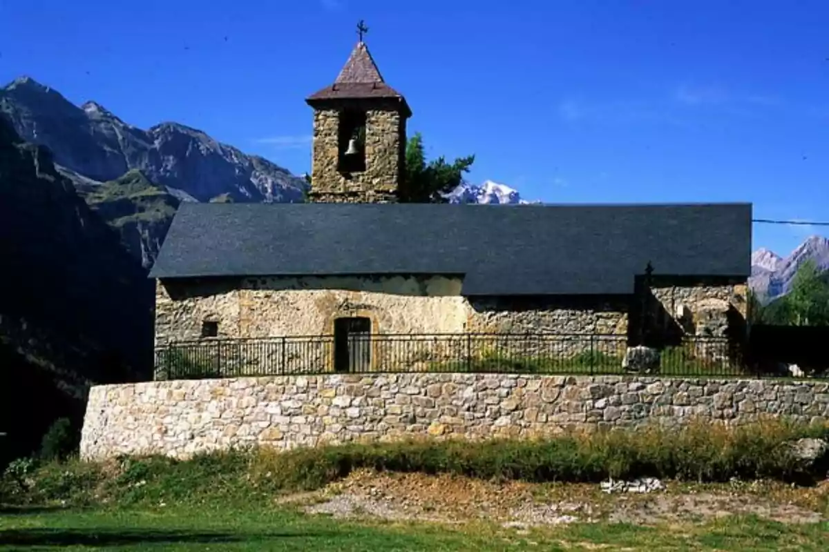 Una iglesia de piedra con un campanario en un entorno montañoso bajo un cielo azul.