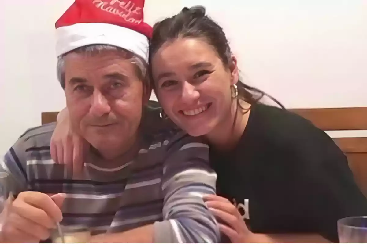 Una persona con gorro de Navidad y otra persona sonriendo mientras posan juntas en una mesa.