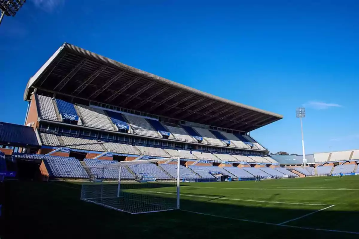 Un estadio de fútbol vacío con gradas y una portería bajo un cielo despejado. Un estadio de fútbol vacío con gradas y una portería bajo un cielo despejado.