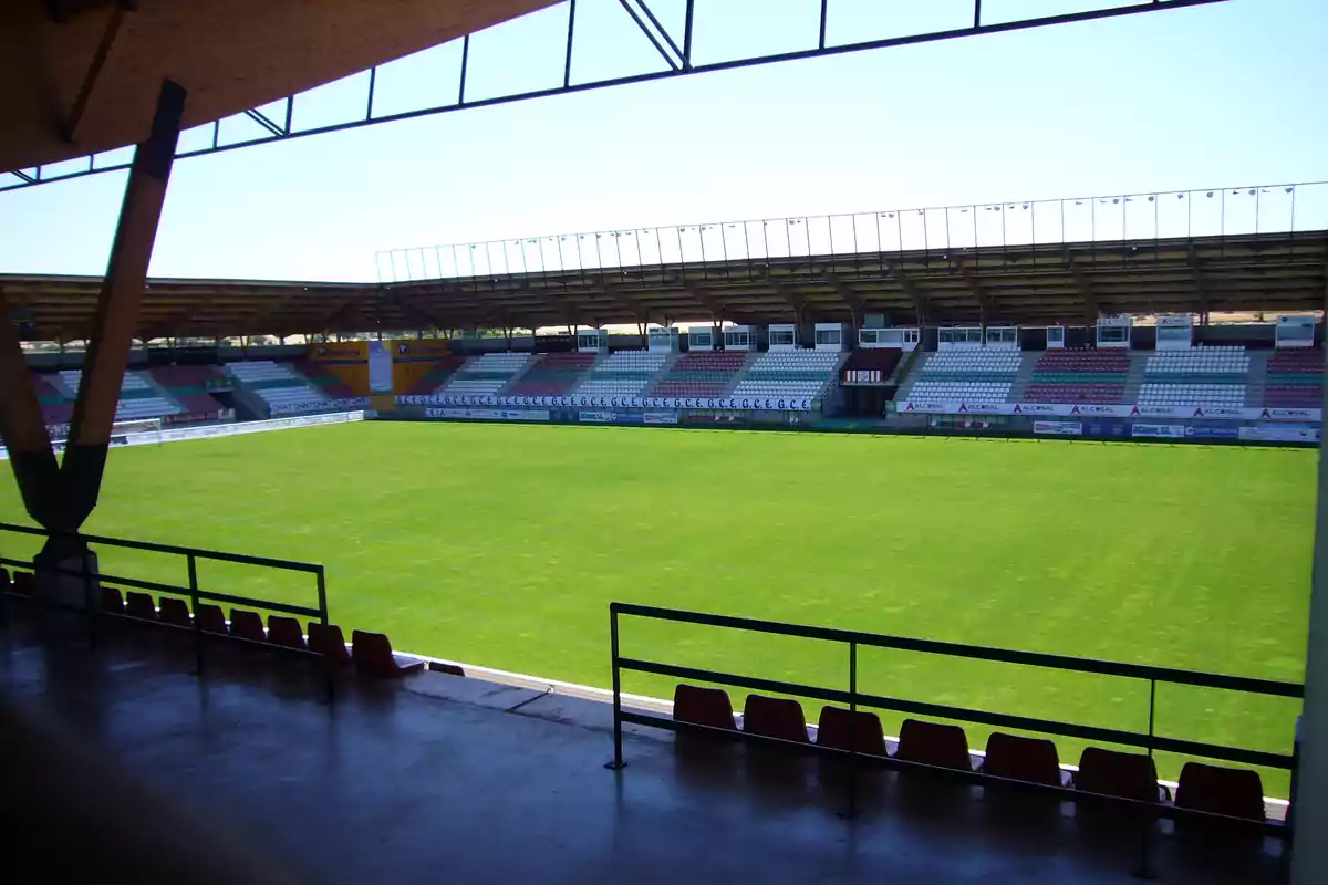 Estadio de fútbol vacío con gradas y césped verde visto desde la tribuna cubierta.