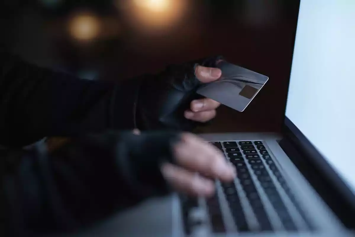 Persona con guantes sosteniendo una tarjeta de crédito frente a una computadora portátil.