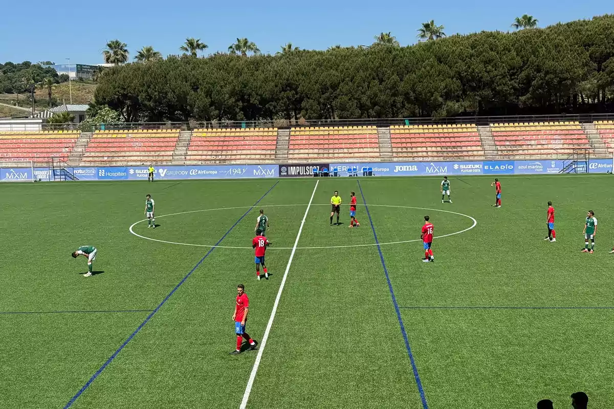 Jugadores de dos equipos de fútbol en el centro del campo listos para iniciar un partido en un estadio con gradas vacías y árboles al fondo Jugadores de dos equipos de fútbol en el centro del campo listos para iniciar un partido en un estadio con gradas vacías y árboles al fondo