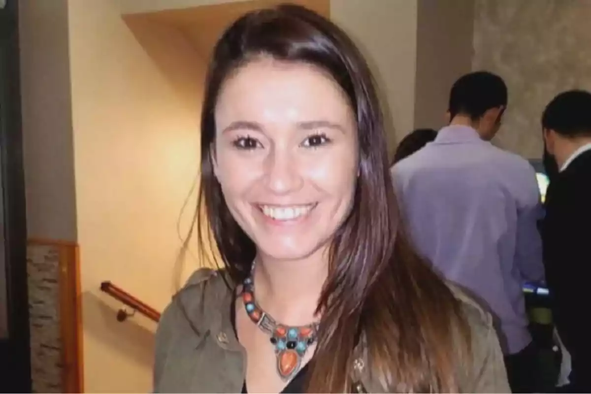 Una mujer sonriente con un collar colorido en un ambiente interior.