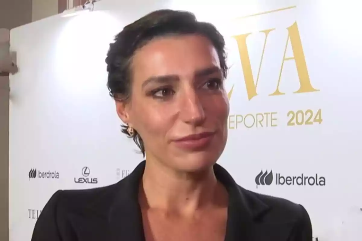 Eugenia Osborne con cabello corto y oscuro lleva un traje negro y está frente a un fondo con logotipos y texto que dice Eugenia Osborne con cabello corto y oscuro lleva un traje negro y está frente a un fondo con logotipos y texto que dice