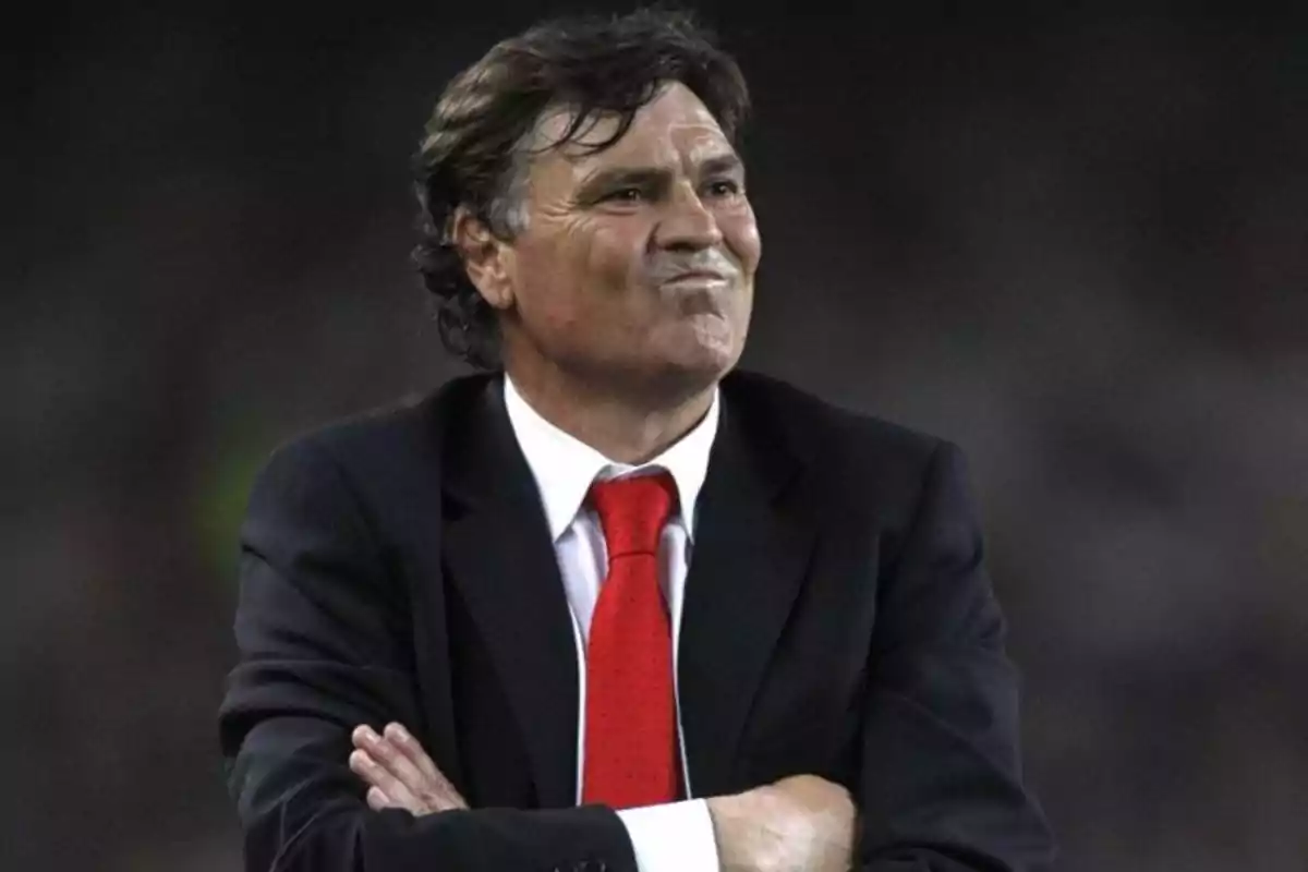 Hombre de cabello oscuro con traje y corbata roja cruzando los brazos y haciendo un gesto pensativo Hombre de cabello oscuro con traje y corbata roja cruzando los brazos y haciendo un gesto pensativo