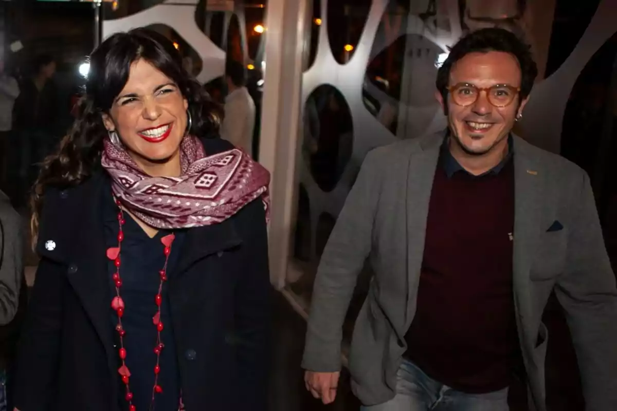 Una mujer y un hombre sonríen mientras caminan juntos en un evento nocturno.