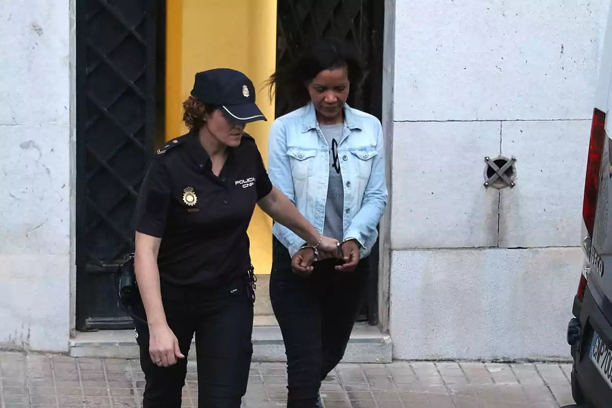 Una oficial de policía escolta a una persona esposada mientras salen de un edificio.