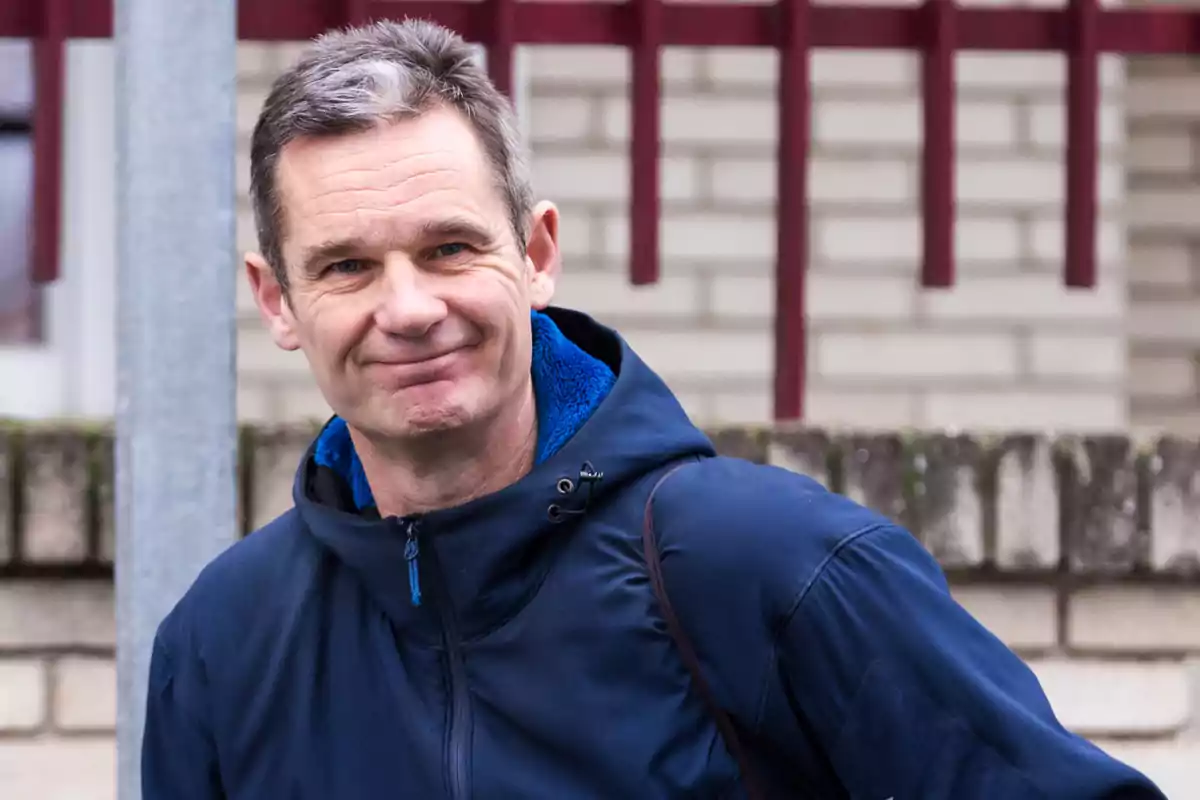 Un hombre con chaqueta azul sonriendo frente a una pared de ladrillos.