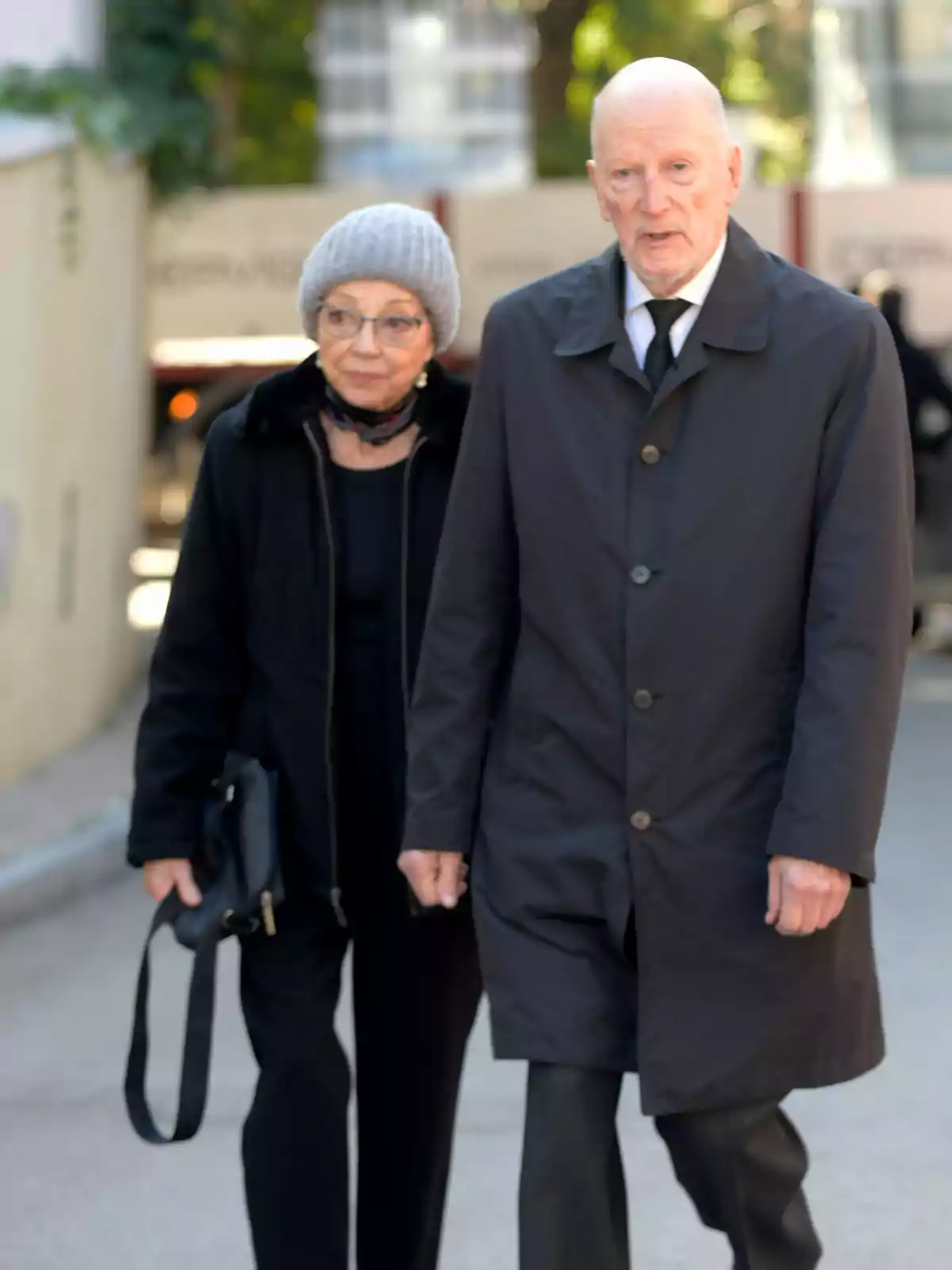 Una pareja de personas mayores caminando juntas, el hombre lleva un abrigo oscuro y la mujer un gorro gris.