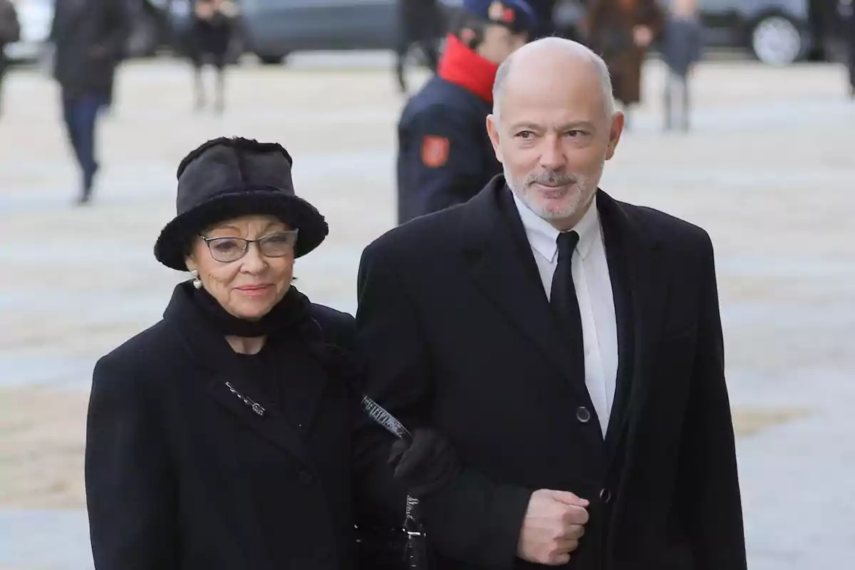 Una pareja vestida de negro camina al aire libre en un evento formal.